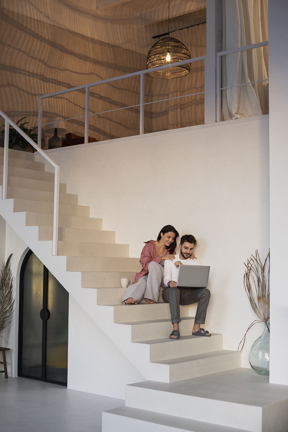 Pareja joven sentada en una escalera moderna mirando un portátil, planificando su futuro hogar