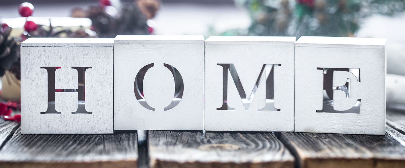 Bloques de madera blancos con la palabra HOME recortada, sobre mesa rústica y decoración de fondo