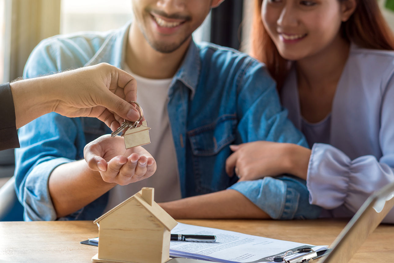 Pareja feliz recibiendo las llaves de su nueva vivienda con contrato y maqueta de casa sobre la mesa