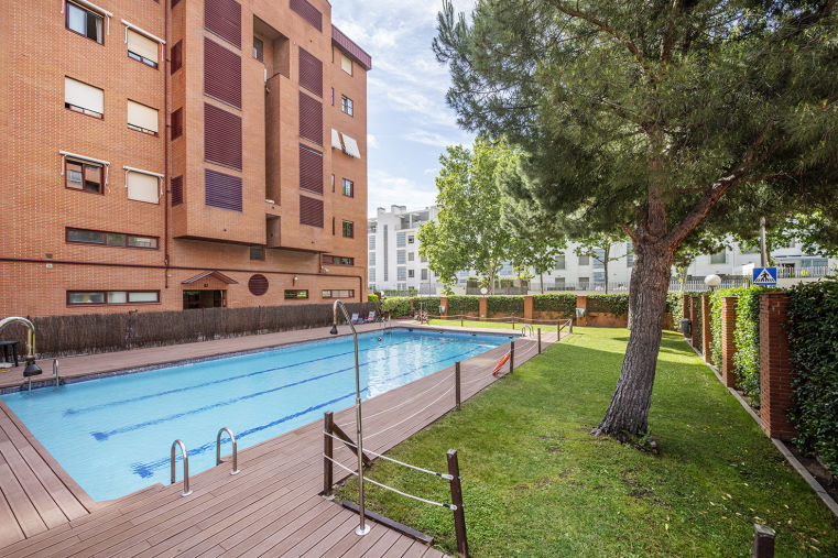 Zona comunitaria con piscina, jardín y edificio residencial de ladrillo en urbanización privada