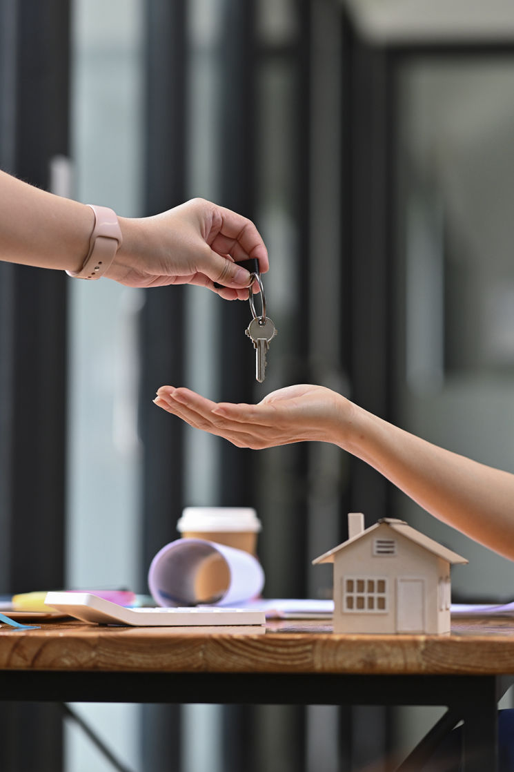 Entrega de llaves entre dos personas con maqueta de casa sobre la mesa, simbolizando la compra o alquiler de vivienda